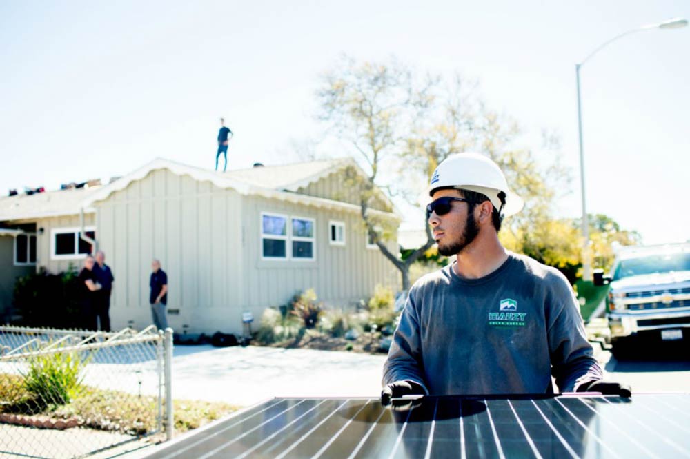 一名太阳能安装工背着太阳能电池板走向一户人家